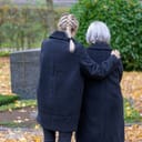 A daughter embracing her mother for comfort at a grave site in the cemetery.
