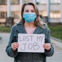 A woman with a face mask holding a piece of paper that says 'Lost My Job'