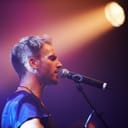 A vocalist singing at a concert with lights shining on him