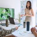 young woman presents ESG topics to a diverse business team in the office, using a laptop linked to a monitor