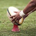A kicker setting a rugby ball on a stand