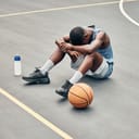 basketball player on the court with water bottle and a ball next to him, showing signs of sports burnout
