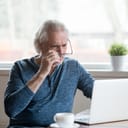 A surprised man taking of his glasses in disbelief while looking at his laptop