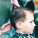 One Cute little boy getting haircut by hairdresser at the barbershop.Side view.Closeup.Toned