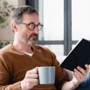 Close up image of a relaxed Caucasian mature man father reading book, preparing for lessons tutoring, enjoying novel at home lying on the sofa couch. Social distance , isolation concept