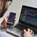 A closeup of a man looking at stock market on his phone and laptop