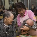 Nurse holding a baby while an elderly man cheerfully looks on