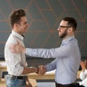 Man congratulating another man with a handshake in an office