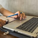 male student using laptop and a pencil while studying in the library