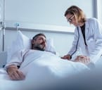 A male patient in bed being overseen by a smiling female doctor