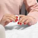 close-up of woman's hands, removing red nail polish with a cotton pad