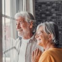 An elderly couple standing by the window looking outside