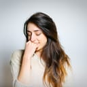 portrait of a shy brunette girl that's slightly smiling and looking down, with her hand close to her face