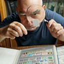 A senior gentleman checking a valuable stamp up close using a magnifying glass.