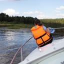A person sitting on a bow wearing an orange life jacket while the boat is leaning to side