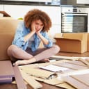 Confused woman sitting on floor in front of a disassembled piece of furniture