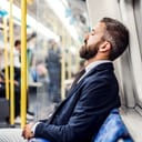 A tired bearded man in a suit sleeping on a bus