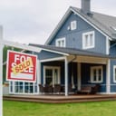 Red "Sold" sign in the garden of a stylish blue house with traditional architecture