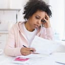 A worried young woman looking at finances at her kitchen table