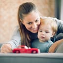young mum and her toddler son playing with a red car toy in their living room