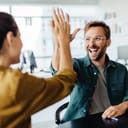 Successful business people giving each other a high five in a meeting. Two young business professionals celebrating teamwork in an office.