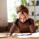 Stressed young afro american woman holding head in hands and feeling demotivated while sitting at her home office and working remotely on laptop. Depressed female student tired of onling learning