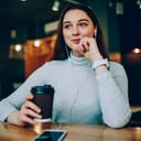 A young woman drinking coffee with her headphones on in a cafe