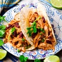 Plated tacos with shredded chicken with parsley and lime on the side