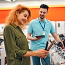Woman trying out a hair straightening iron while a shop clerk is waiting to assist her
