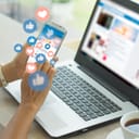 Young woman on smartphone with a laptop in the background