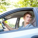Close-up of a focused male teenager driving a car in reverse, carefully watching the road and traffic.