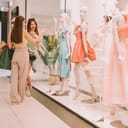 two sisters at a shopping mall, one pointing at dresses and explaining something to the other