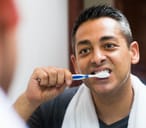Man brushing his teeth looking at his reflection in the mirror