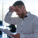 An upset man reading a text from a piece of paper while holding a pen