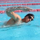 A man wish a swimming cap and goggles swimming in an Olympic pool
