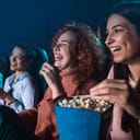 Three friends at a cinema watching a funny movie and eating popcorn