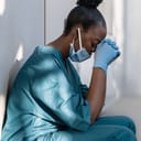 An exhausted nurse squatting with her back leaning on a wall and head in hands