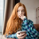 A young woman holding a phone with a nervous look on her face