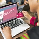 An over the shoulder view of a woman make an online purchase on her laptop while holding a credit card