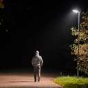 A man with his hands in his pockets walking past a lamp post alone at night