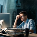Casual tired office worker sitting at desk using computer and doing overtime project in lamplight.