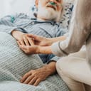 Close-up of an older dying man holding his wife's hands.
