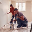 Couple Painting Test Squares On Wall As They Decorate Room In New Home Together