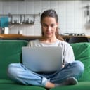 a young woman sitting on a green sofa at home and using laptop