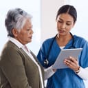 A nurse talking to an older woman while holding a tablet