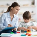 Woman taking notes as she watches a young boy play with toy bricks