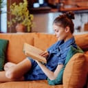 Woman relaxing on an orange couch at home and reading a book