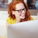A closeup young woman trying to hold her laughter while seated at an office desk