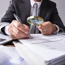 close-up of an investigator examining reports with a magnifying glass and pen in his office