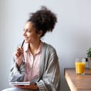 Portrait of a happy young woman sitting at home with pen and paper